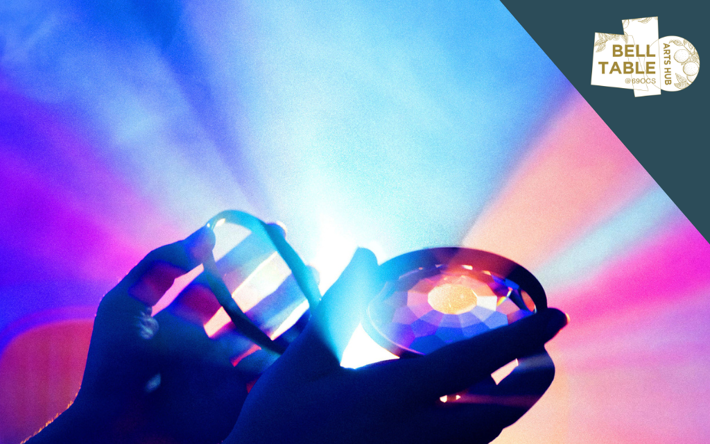 Silhouette of pair of hands holding up a circular crystal with shades of blue, purple and pink shining out around.