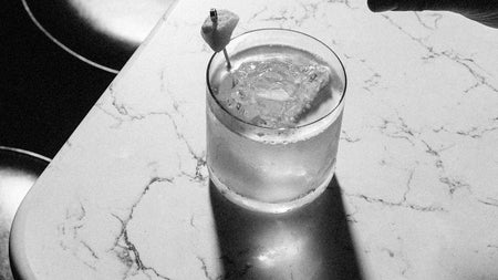 A cocktail in a short glass on the corner of a white marble bar counter