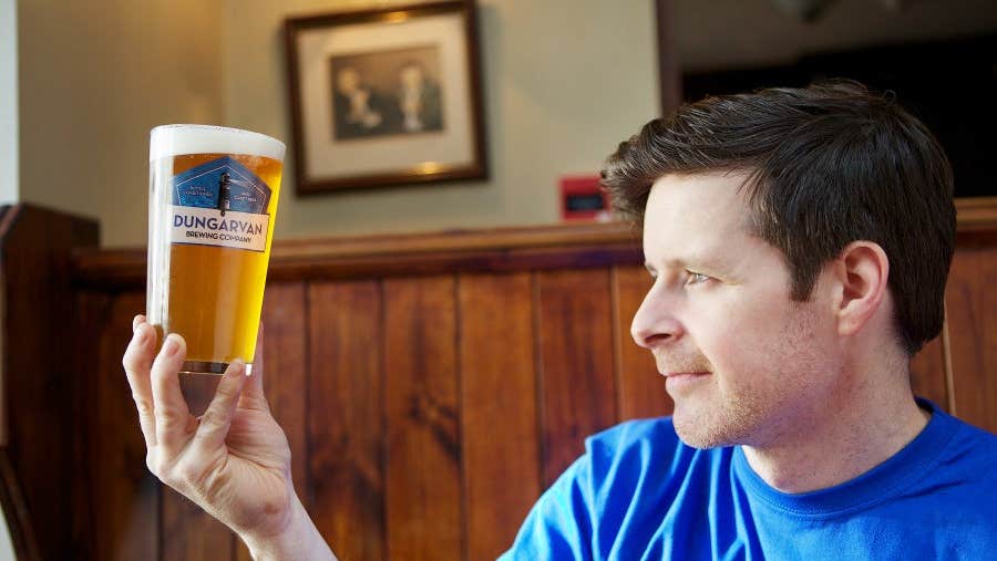 A man holds a pint of Dungarvan Brewery beer up to the light