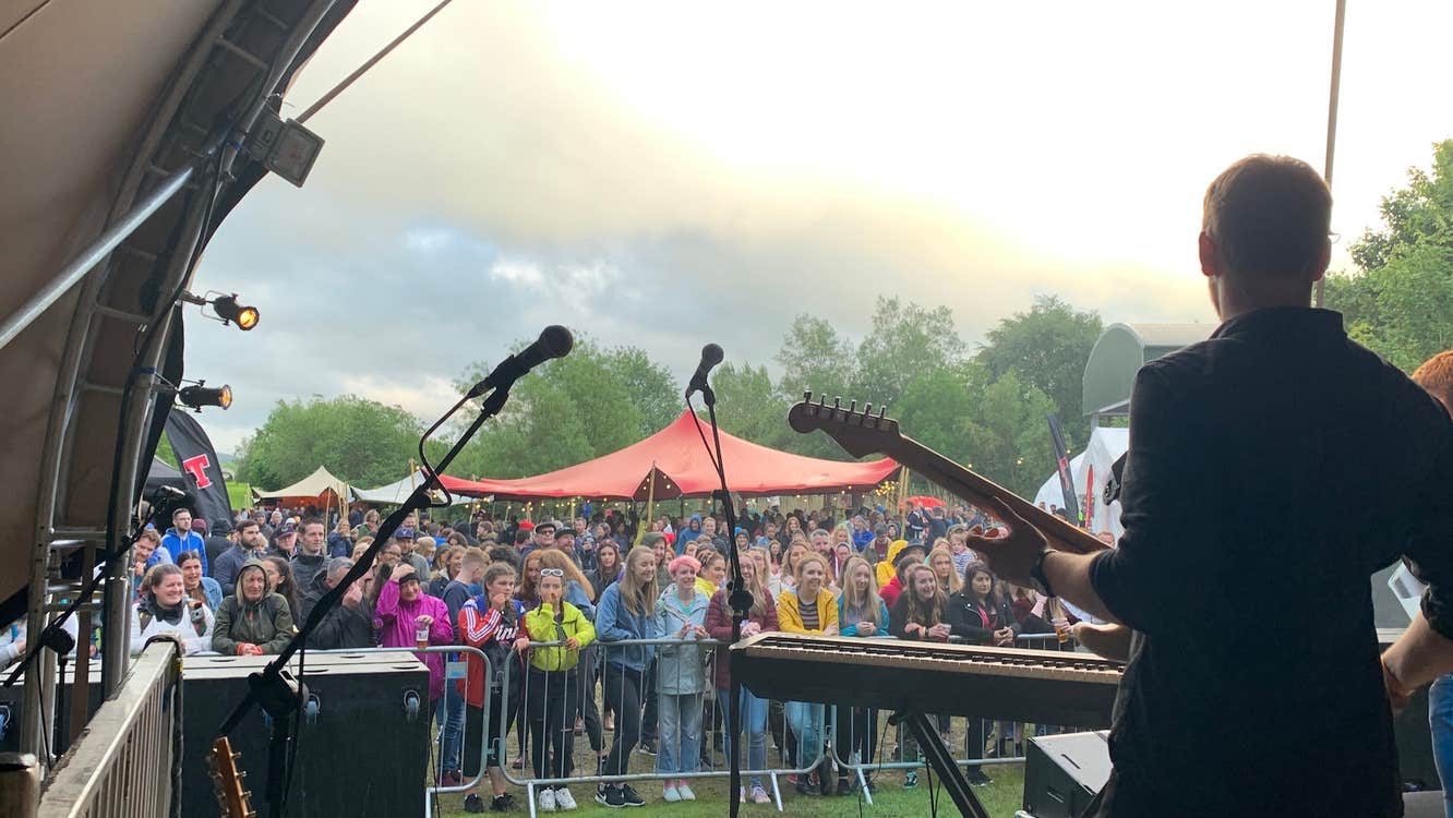 View from an outdoor stage behind a musician looking out at a small crowd on a cloudy day.