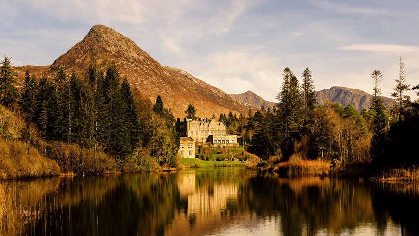 An autumnal morning view of Ballynahinch Castle from across the lake with trees and hills in the background