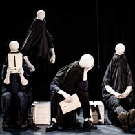 4 plain figures on a stage dressed all in black with plain, small, round blank heads