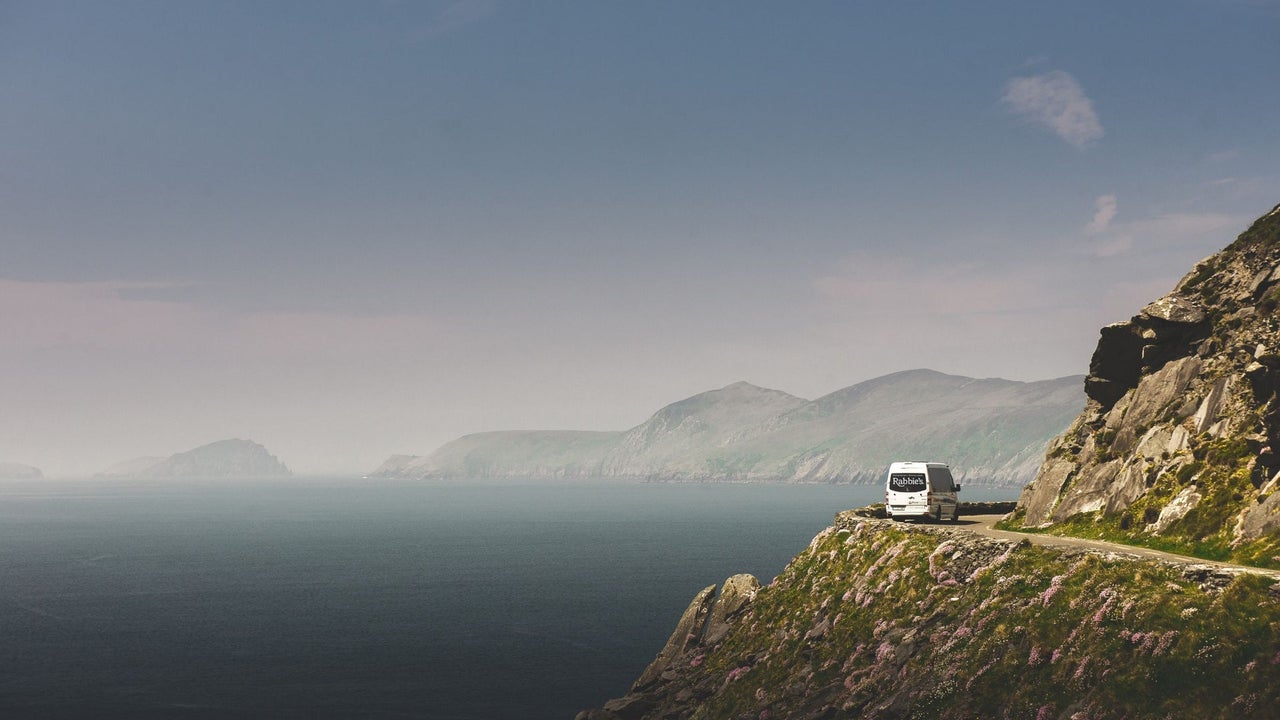 A Rabbies white mini bus driving along a cliff road beside the sea