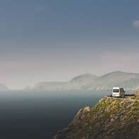 A Rabbies white mini bus driving along a cliff road beside the sea