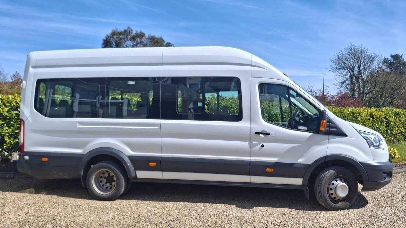 Side view of a white minibus parked on gravel with a blue sky in the background