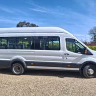 Side view of a white minibus parked on gravel with a blue sky in the background