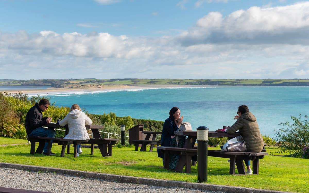 People sitting at picnic tables having lunch with a coastal view in the background