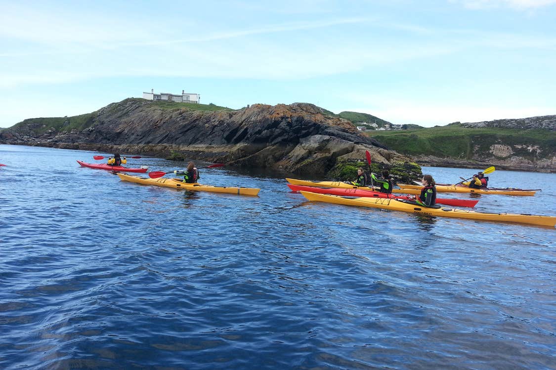 Group of kayakers paddling beside rocks in the sea.