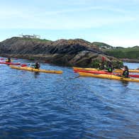Group of kayakers paddling beside rocks in the sea.