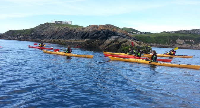 Group of kayakers paddling beside rocks in the sea.