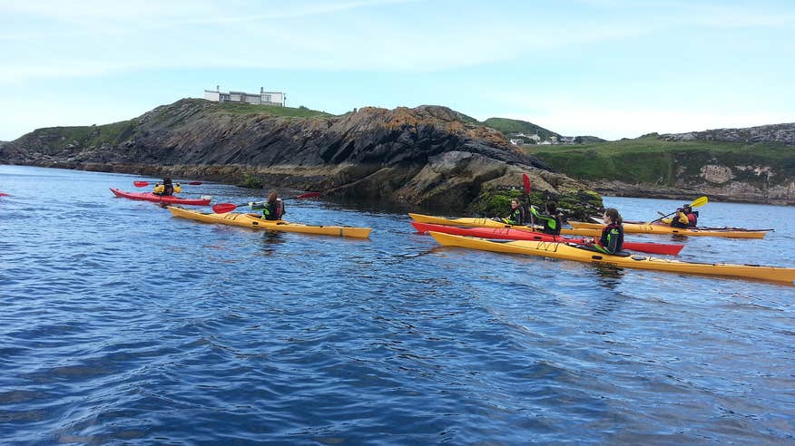 Group of kayakers paddling beside rocks in the sea.