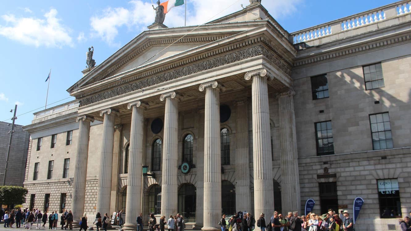 A walking tour group and guide outside a stately building on a busy city street
