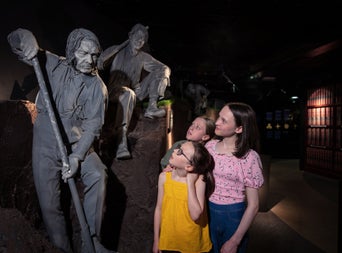 Three kids looking at a gravedigger statue as part of the City of the Dead exhibition