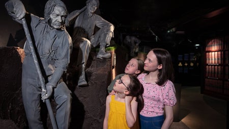 Three kids looking at a gravedigger statue as part of the City of the Dead exhibition