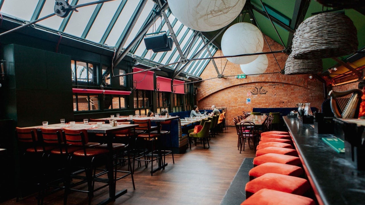Bar area with exposed brick walls skylights red seating and large pendant lights above the tables