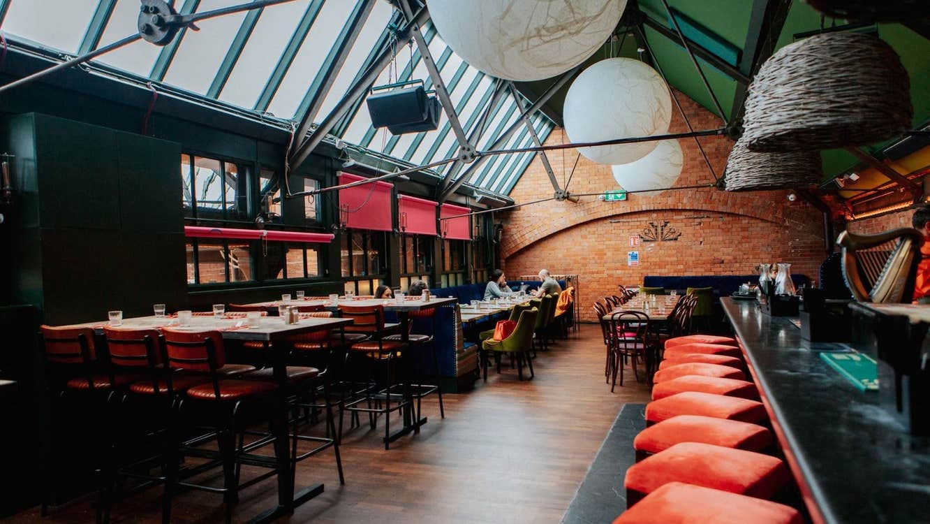 Bar area with exposed brick walls skylights red seating and large pendant lights above the tables