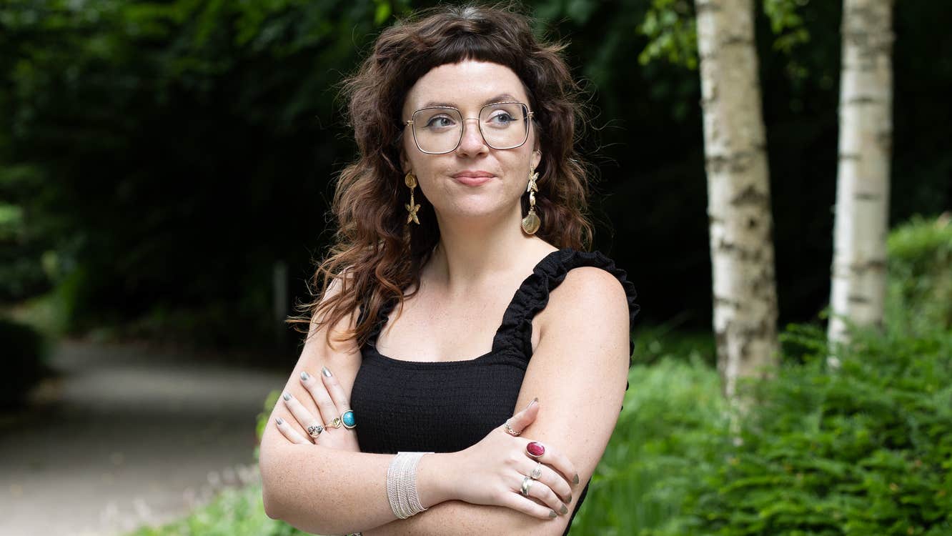 A smiling Ava Hayes is standing outdoors with her arms crossed.