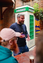 A tour guide standing beside an old fashioned phone box while speaking to a tour group