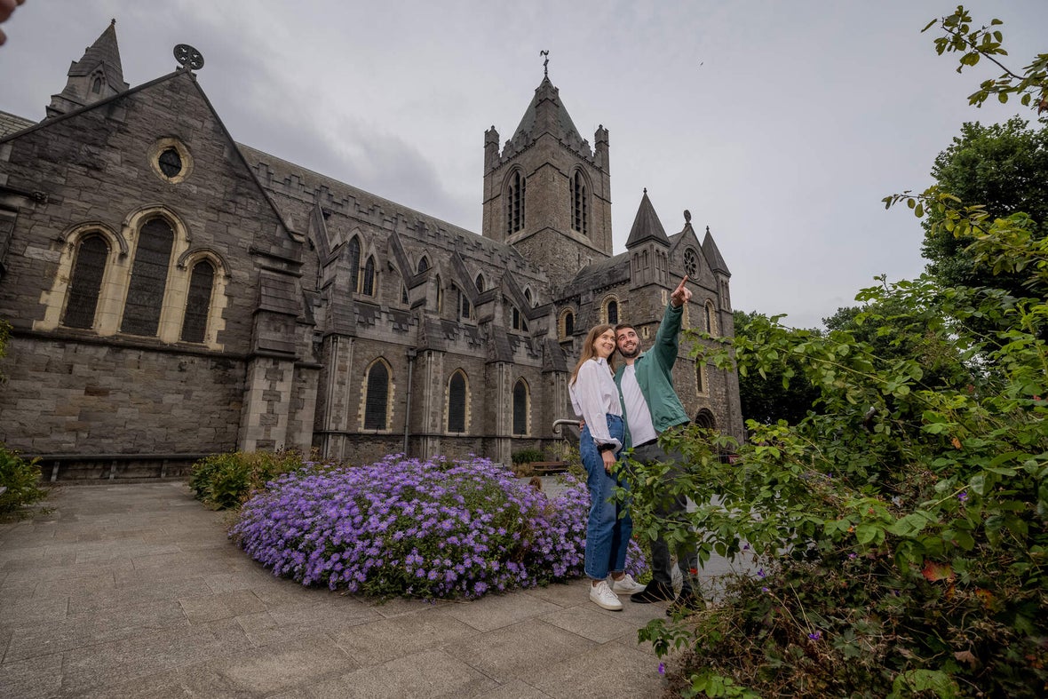 A couple standing in the gardens of Christ Church Cathedral, pointing to something off camera and smiling.