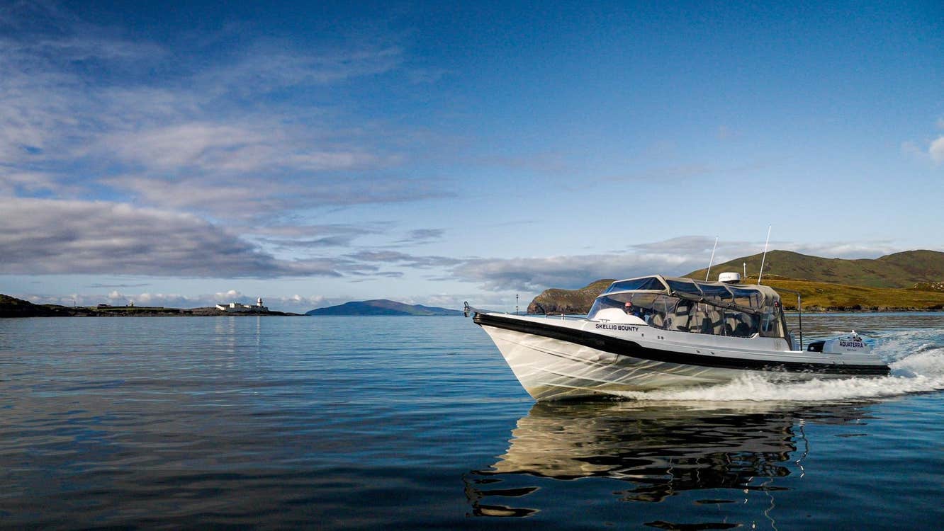 White boat sailing on calm water with cliffs and a lighthouse in the background