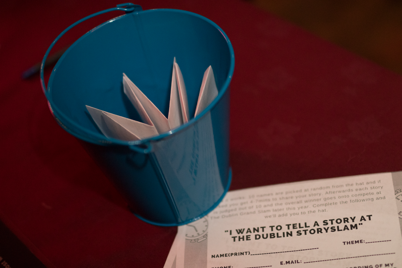 How to share a personal true story about your mental health…safely. A blue, shiny metal bin contains a folded piece of beige coloured paper with another piece with writing on in front of the bin on a dark red floor.