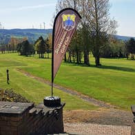 Image of two banner flags at the entrance to Strokestown Golf club with golf course in the background 