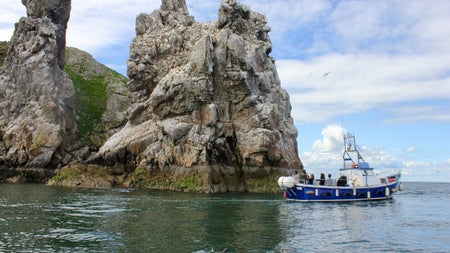 A small passenger boat sailing past some cliffs