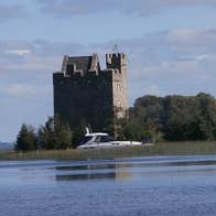 A castle on the lake with a boat passing by Secret Escapes Ireland, Clare