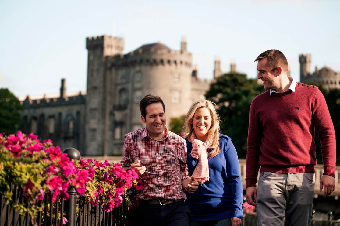 A group of friends laughing outside Kilkenny Castle beside some flowers