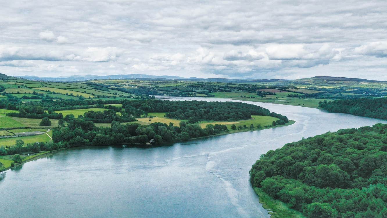 Aerial view of a bend in a river flowing between green landscape
