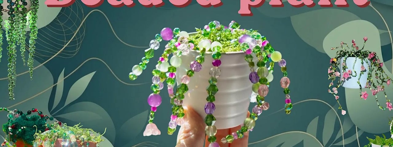 A hand holding up a small white pot with different coloured beaded strings trailing down the sides.