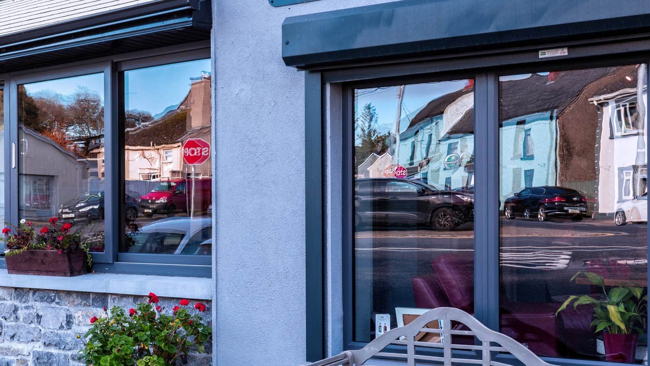 Blue building on a footpath with a seat outside and cars reflected in the windows