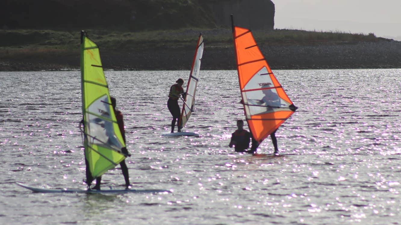 People surfing at sea with yellow and orange sails