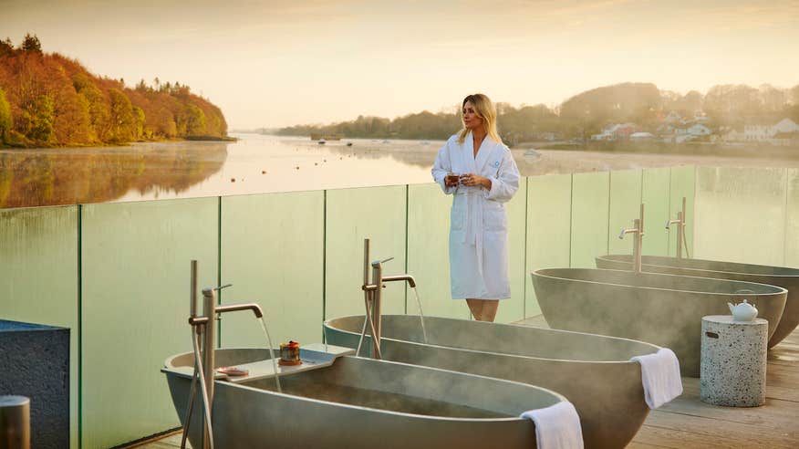 Woman in an Ice House Hotel bathrobe leaning on the glass railing overlooking the water in Ballina standing beside seaweed baths.