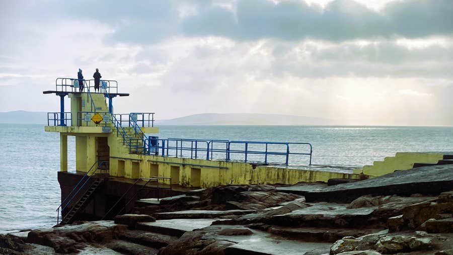 View of diving platforms at 2 different levels set over the water on rocks.