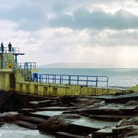 View of diving platforms at 2 different levels set over the water on rocks.