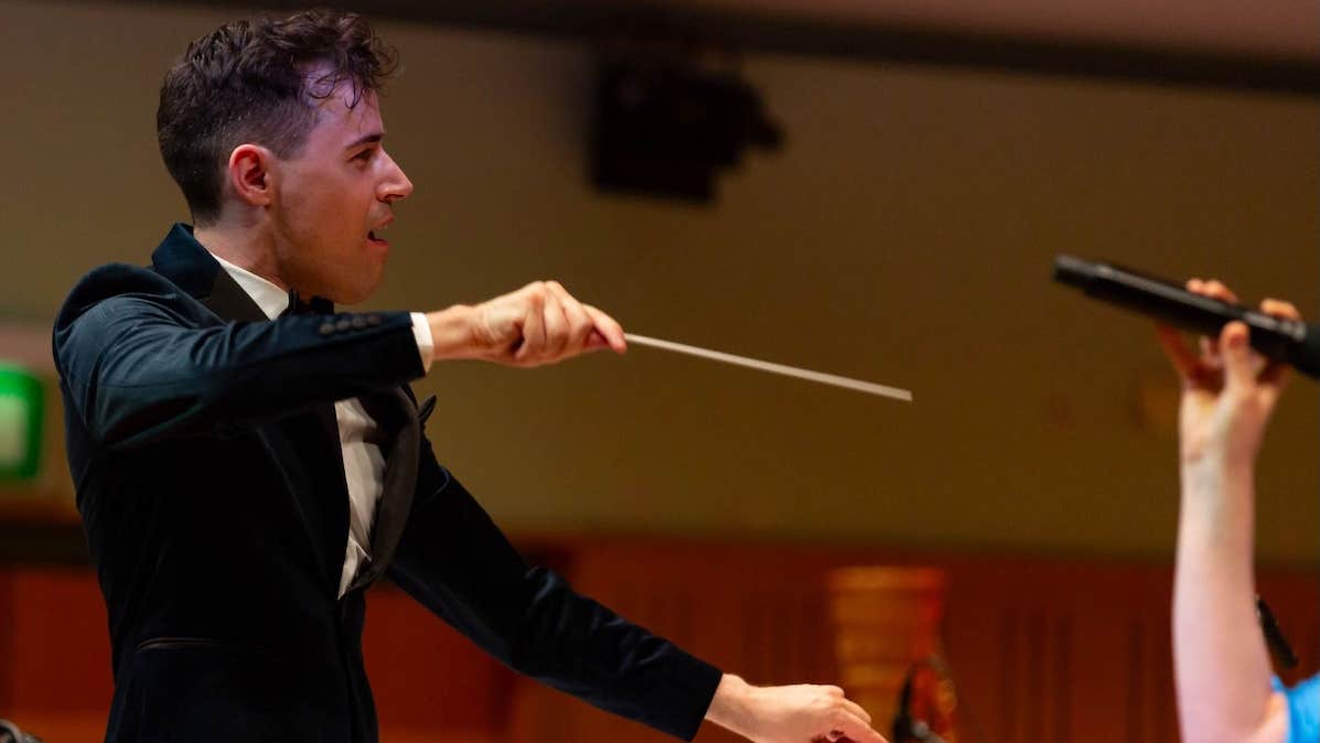 An animated man in evening suit conducting holding a slim baton