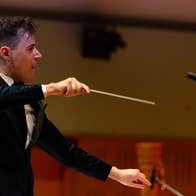 An animated man in evening suit conducting holding a slim baton