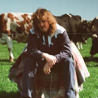 Kean Kavanagh - a man in country style shirt is seated in a field with cows behind.