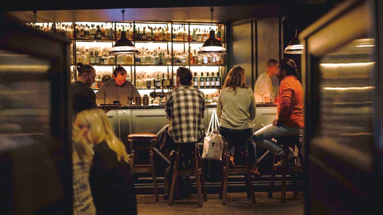 People sitting on stools at a bar in low light