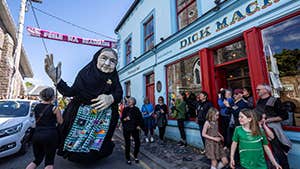 Large puppet of old woman in black as part of parade in a town street.