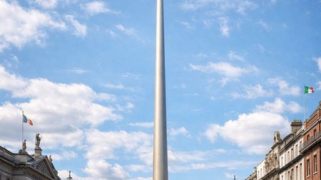 A tall metallic spire landmark on a city street