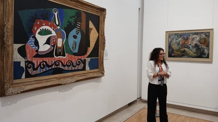 Guide standing in front of two paintings in a room with white walls and wooden floors