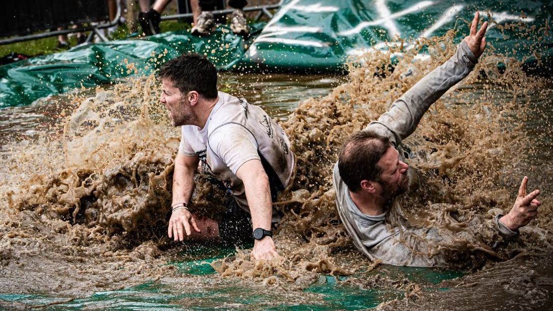 2 men are splashing through man made area of muddy water