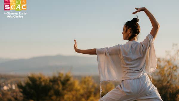 A woman dressed in white in a movement pose with arms outstretched outdoors with distant view.