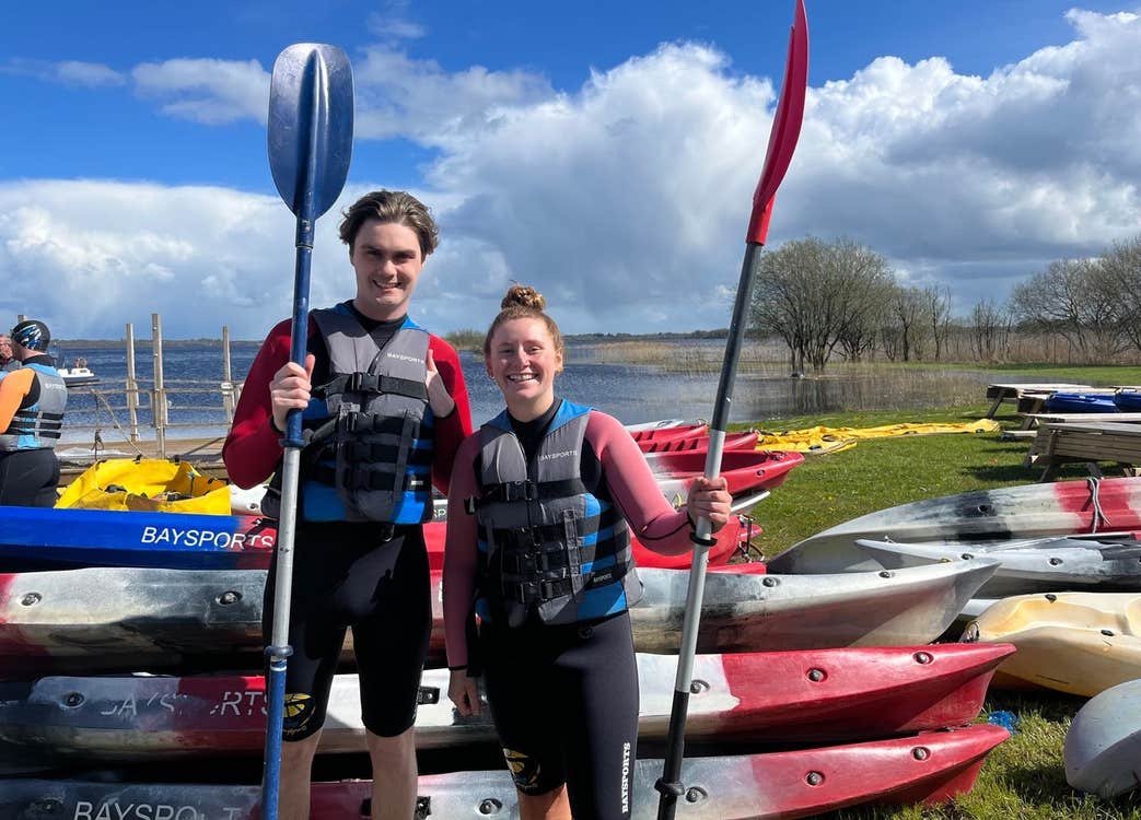 A boy and girl holding their paddles standing next to kayaks with Baysports