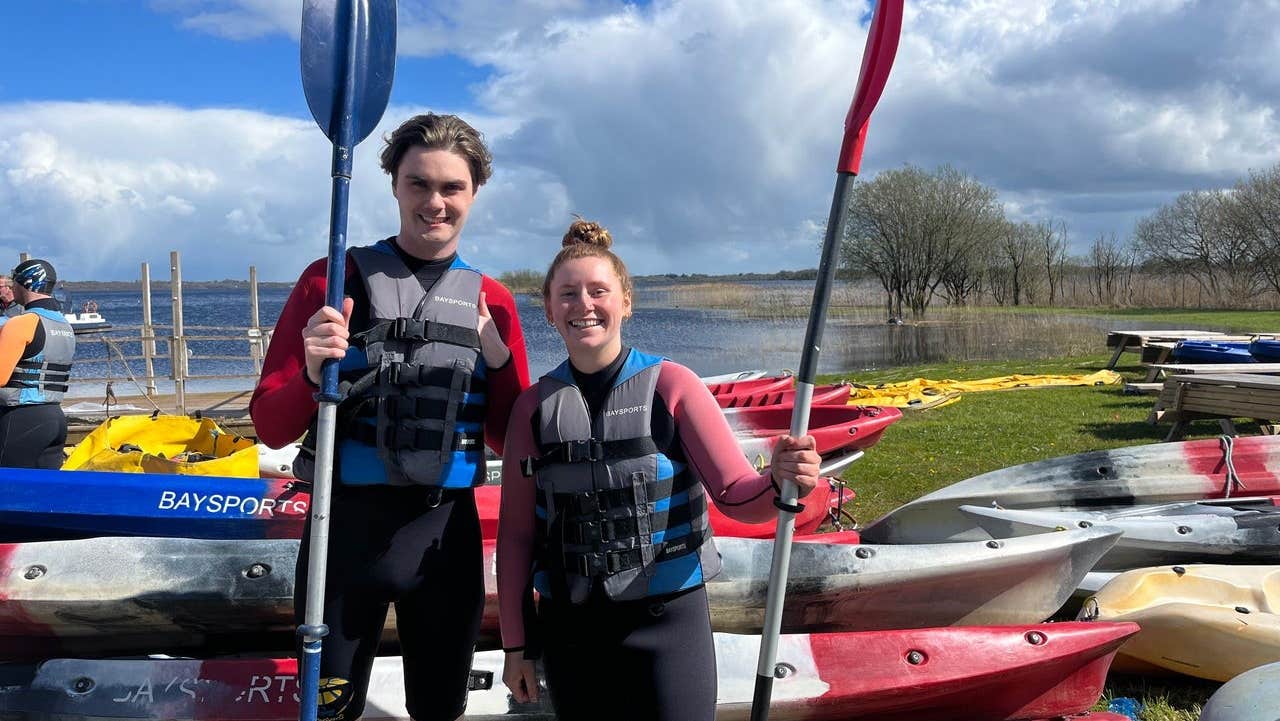 A boy and girl holding their paddles standing next to kayaks with Baysports