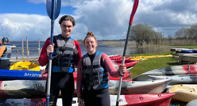 A boy and girl holding their paddles standing next to kayaks with Baysports