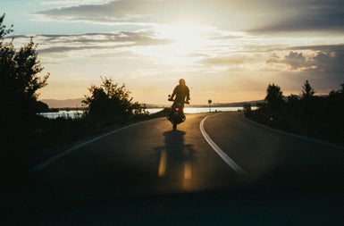 A lone motorbike and rider on a road at sunset