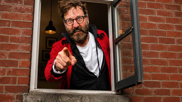 An angry looking man pointing a finger is at a small open window